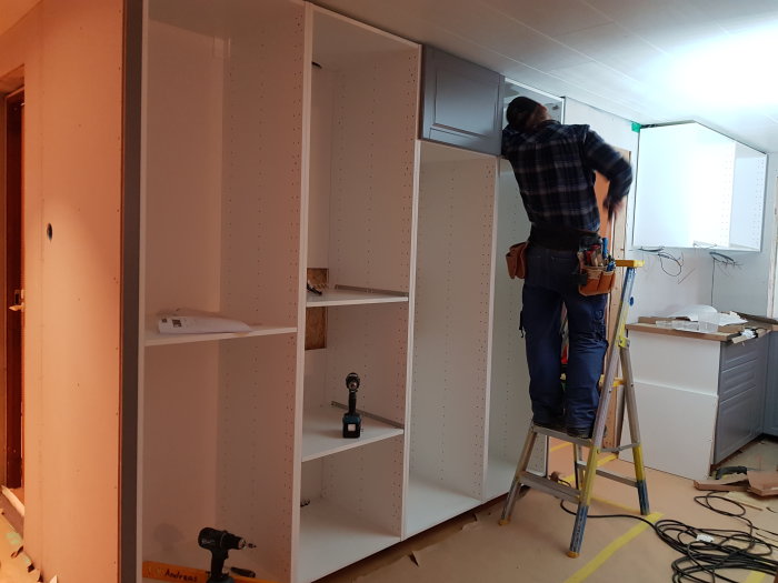 En person monterar köksskåpstommar i ett rum under renovering.