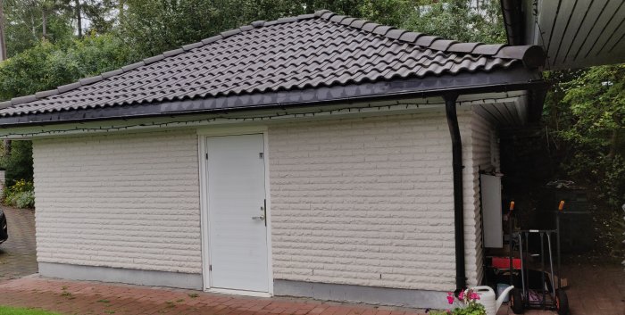 Garage med vit tegelvägg och svart sadeltak med frågan om möjligheten att lyfta taket.