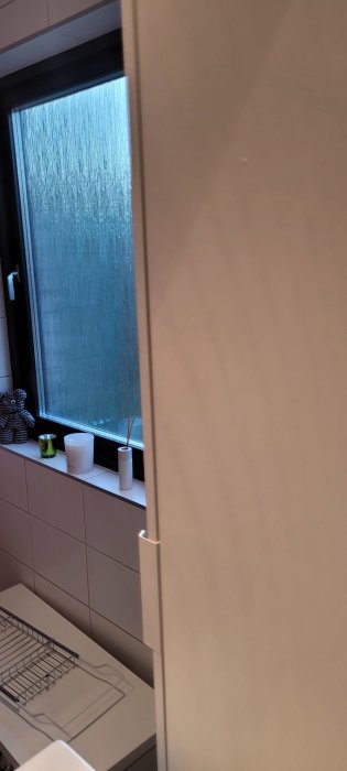 Del av ett modernt badrum med matta kakelväggar och förvaring sett genom dörrspringan.