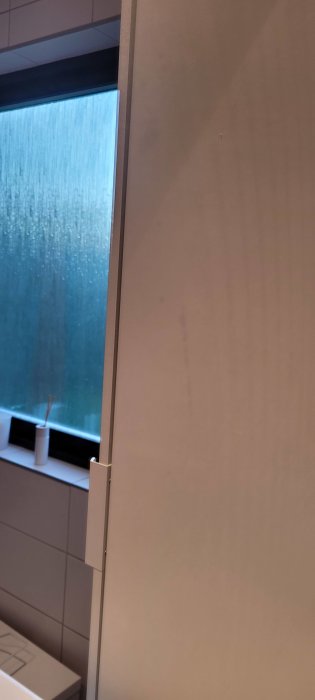 En bild av ett fönster med frostat glas och en del av en vit köksinredning.