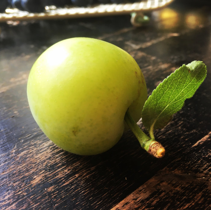Omoget grönt äpple med löv på ett träbord, används för att göra plommonkräm.