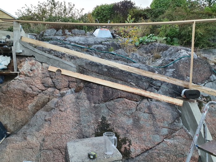 Uppsatt träbräda på ett byggprojekt beläget på en klippa med betongfot och verktyg synliga.