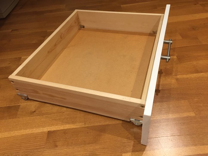 Träram till en låda med MDF-botten och monterade metallbeslag på parkettgolv.