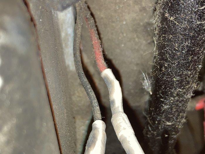 Närbild av två lösa kablar i en maskins motorutrymme, dammiga och med oisolerade ändar.