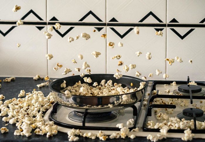 Popcorn som hoppar ut ur en stekpanna på en spis, vilket skapar röra i köket.