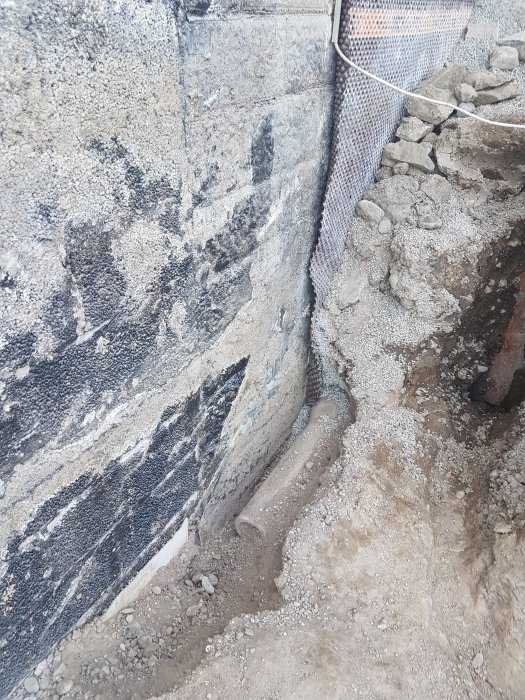 Grävd grop vid husgrund visar ett igensatt cementrör och ett onödigt plaströr med hål i botten.