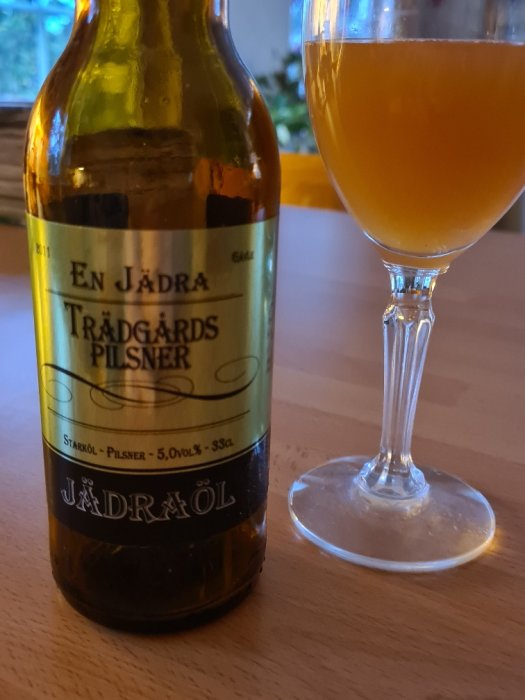 En Jädra Trädgårdspilsner ölflaska bredvid ett glas med öl på ett bord.