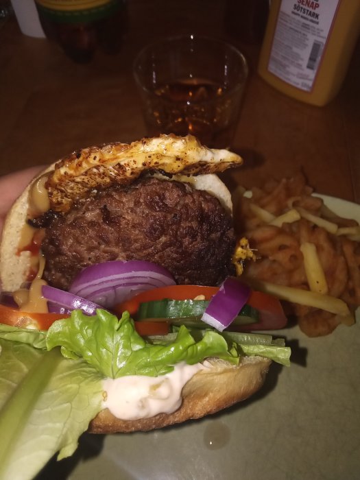 Hemgjord burgare med sallad, tomat, rödlök och stekt ägg, serverat med pommes frites och senap på sidan.
