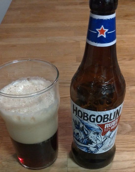 En flaska Hobgoblin Ruby Beer bredvid ett glas med öl och skum topp.