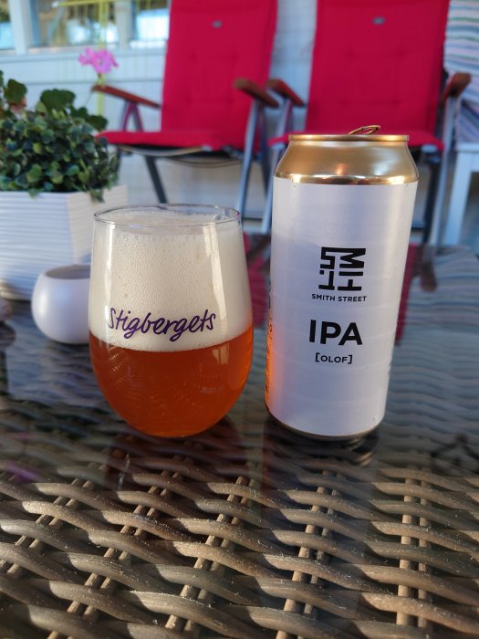 Ett glas öl med skum och en ölburk på ett bord, med röda stolar i bakgrunden.