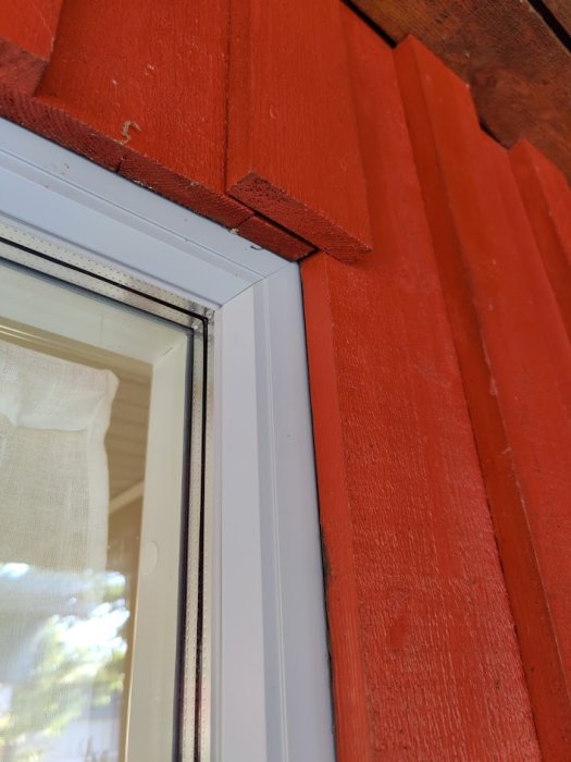 Rött hus med stående lockpanel utan yttre fönsterfoder, närbild på fönster och fasad.