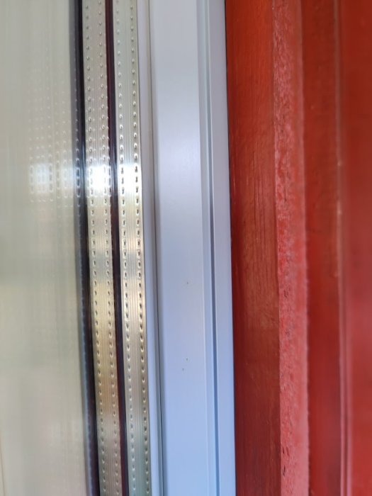 Närbild på fönsterkarm utan yttre fönsterfoder mot en röd fasad.