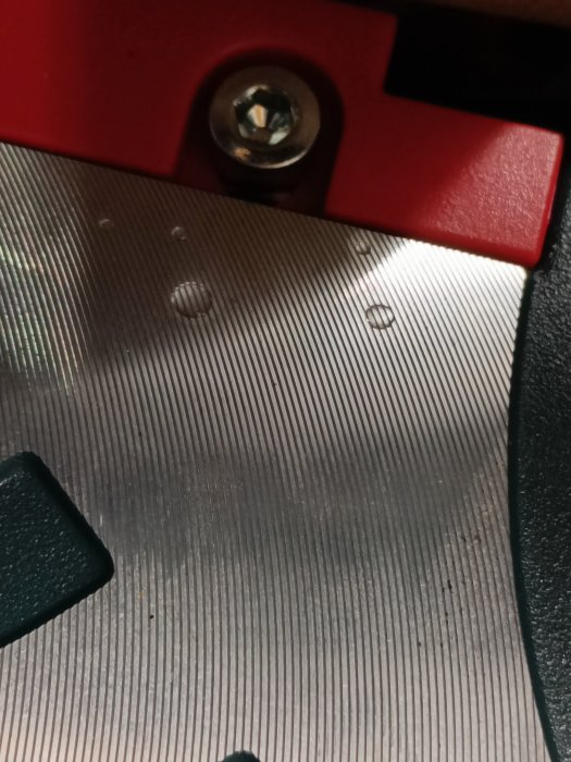 Närbild på en strukturerad metallisk yta med en röd kant och en skruv.