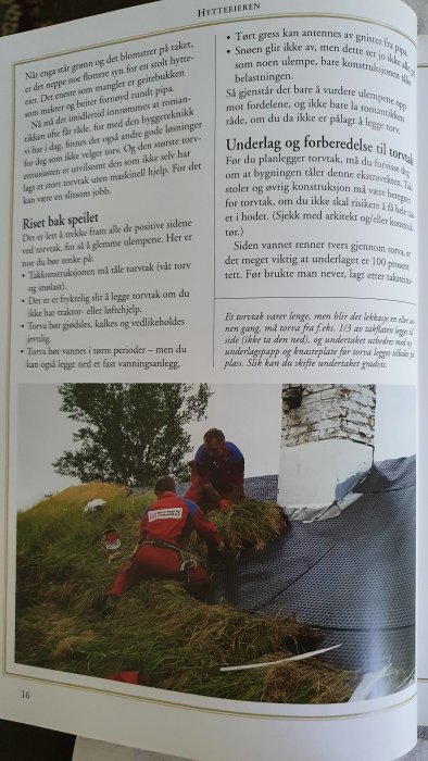 Två personer lägger torv på ett traditionellt tak, nära skorstenen, iklädda röda arbetskläder.
