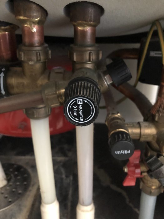 Säkerhetsventil på vattenvärmare med texten "NATUR GAS" omgiven av kopparledningar och ventiler.