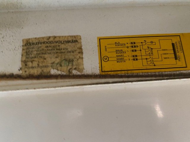Gamla, nedslitna etiketter med teknisk information på en köksfläkt.