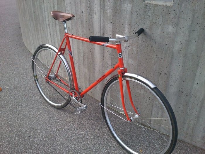 Custombyggd cykel med orange ram och Duomaticnav, parkerad mot betongvägg.