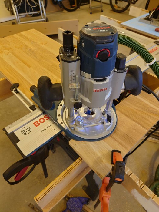 Bosch överhandsfräs monterad på träpanel i verkstad med klämmor och linjaler.
