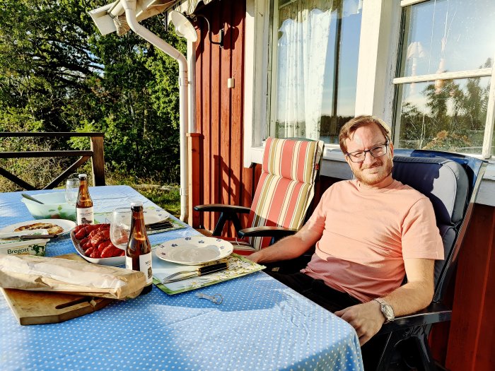 Man sitter vid uteplatsbord med frukt, mat och dryck på en solig dag.