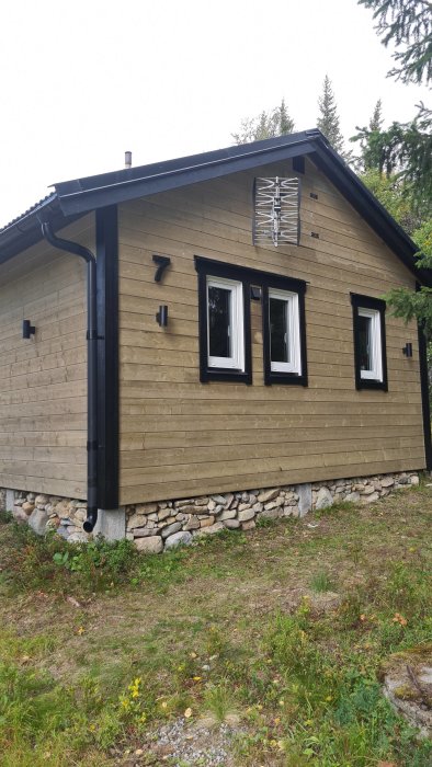Ett hörn av ett hus med olika nyanser av träpanel och svarta fönsterramar, nyligen behandlad fasad.