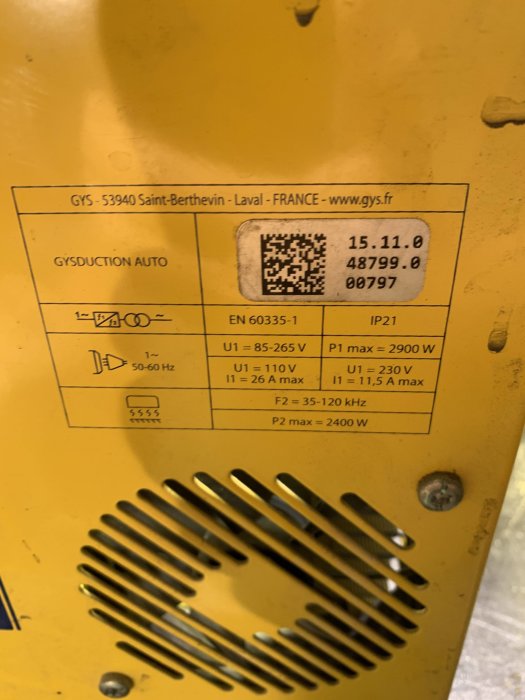 Närbild av en gul maskinplåt med tekniska specifikationer, QR-kod och ventilationsgaller.