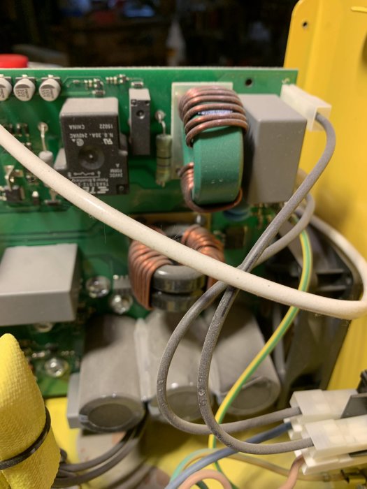 Närbild av en elektronisk krets med spolar, kondensatorer, och kablar inuti en anordning.