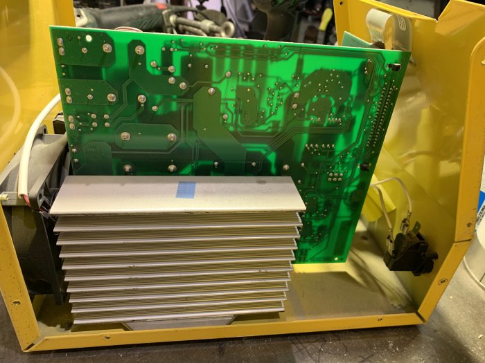 Öppen elektronisk apparat med synligt kretskort och kylflänsar inuti ett gult metallhölje.