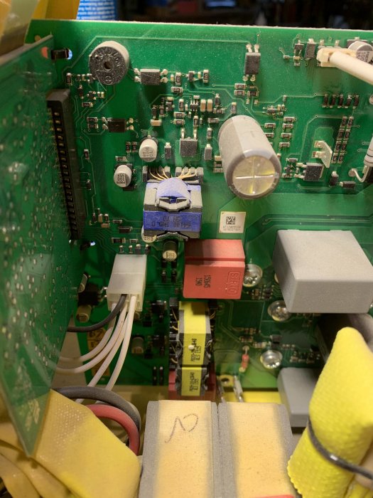 Detaljerad bild av elektronik inuti en apparat med grönt kretskort, kondensatorer, kablar och transformatorer.