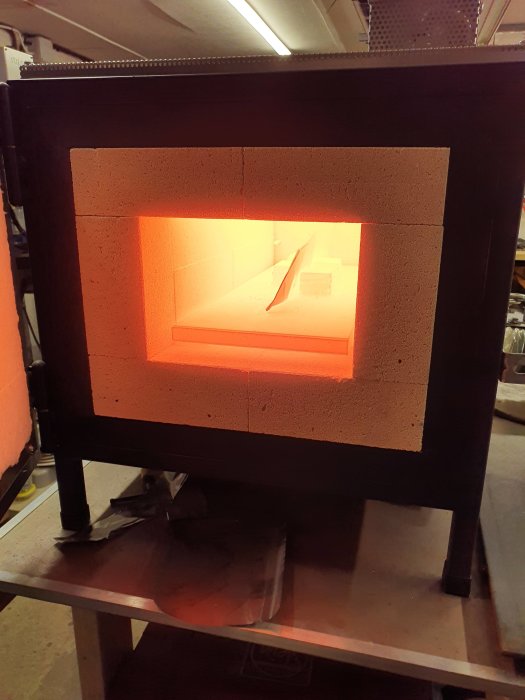 Knivblad upphettas i en öppen smidesugn med glödande ljus inuti.