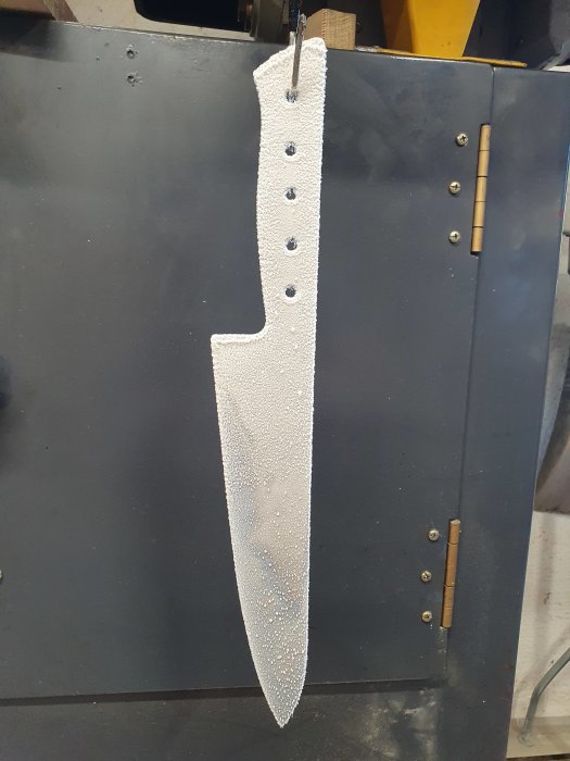 Metallblad täckt av små vita kvävekristaller hängande på en svart yta med skruvar.