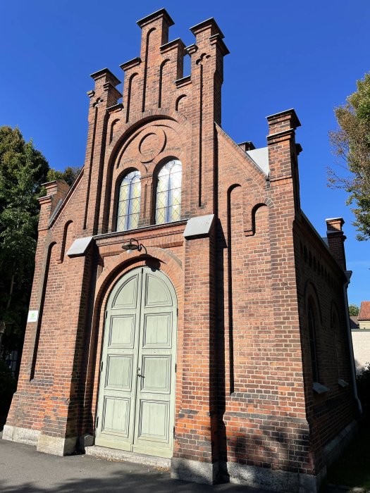 Gammal tegelbyggnad med bågformad dörr och dekorativa tegelgavlar mot klarblå himmel.