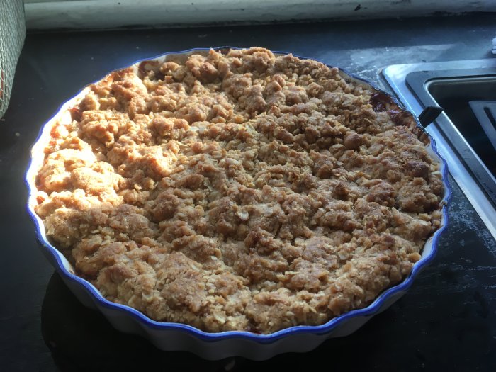 Nybakad äppelpaj med smuligt täcke i blå keramikform på köksbänk.