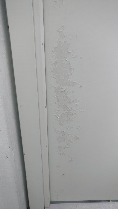Flagnande vit färg på en balkongdörr i närbild.