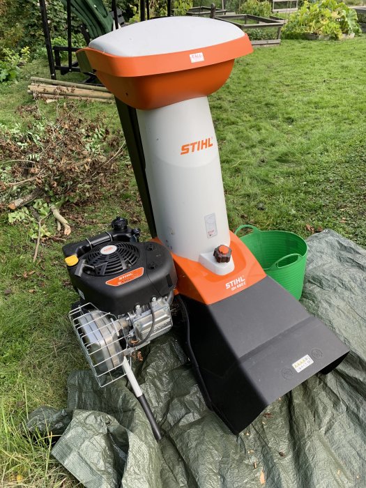 Stihl GH 460C kompostkvarn placerad på gräs med grenar i bakgrunden.