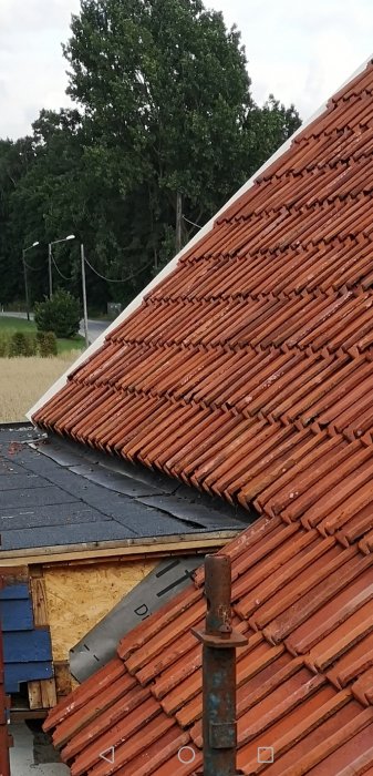 Sadeltak möter platt papptak med vikt plåt vid husets tillbyggnad.