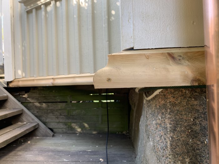 Ny träbalk installerad som stöd under en vit husvägg med stentrappa i bakgrunden.
