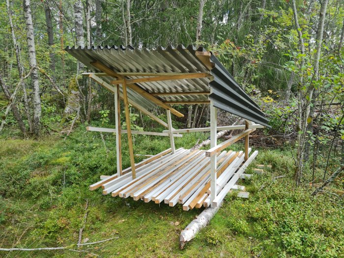 Nytt virkesförråd under konstruktion i skogsmiljö, med trästomme och takplåtar.