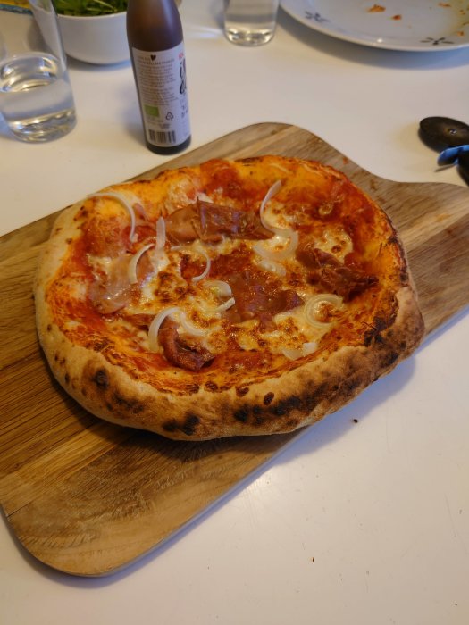 Hemlagad ananaspizza med salami och lök på en skärbräda, bakgrunden visar ett vitt köksbord.