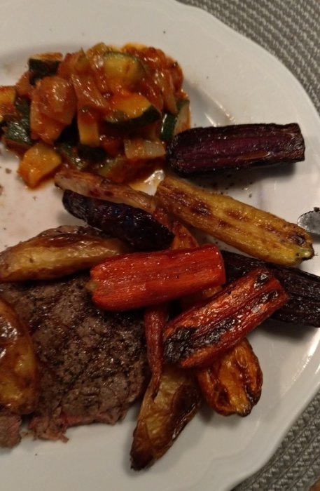 Entrecote med rostade morötter i olika färger och ratatouille på en tallrik, redo för måltid.