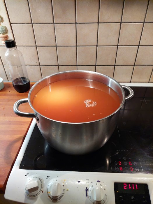 Stor kastrull med orangefärgad vätska på en induktionshäll, eventuell pastörisering.