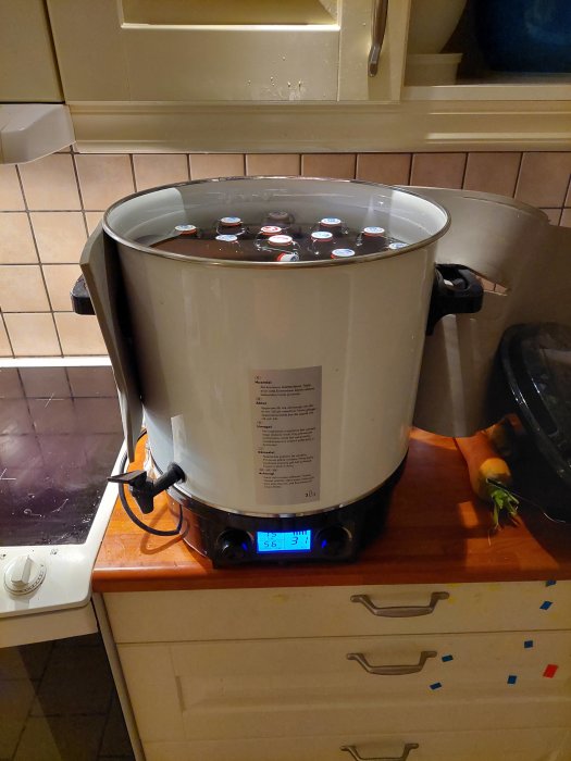 Pastöriseringsapparat fylld med glasflaskor på köksbänk, digital display visar temperatur.