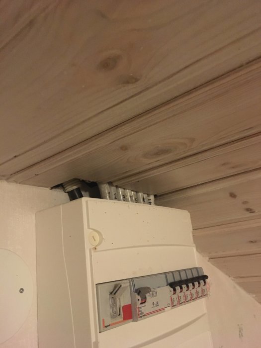 Stort hål i skarven mellan träpaneltak och vit elcentral, potentiell ingång för flugor.
