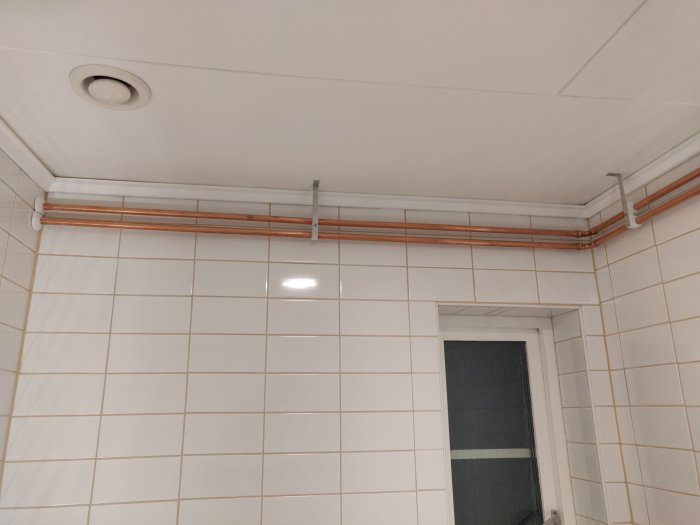 Nymålat badrumstak med vita lister och synliga kopparledningar längs med väggarna.