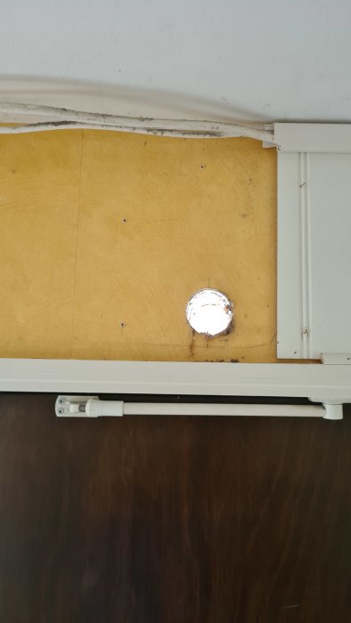 Ett hål i en gul trävägg med synliga rörledningar och elinstallationer, behov av tätning.