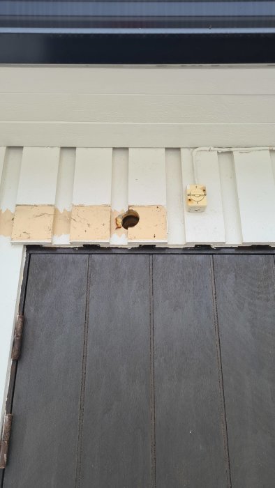 Hål i träfasaden där en LLVP har tagits bort, isolering synlig, bredvid eluttag.