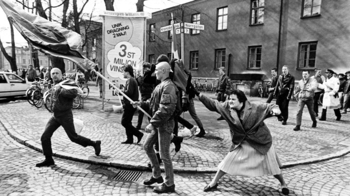 Historisk svartvit bild av en demonstration på gatan från 1985 med människor som bär skyltar och flaggor.