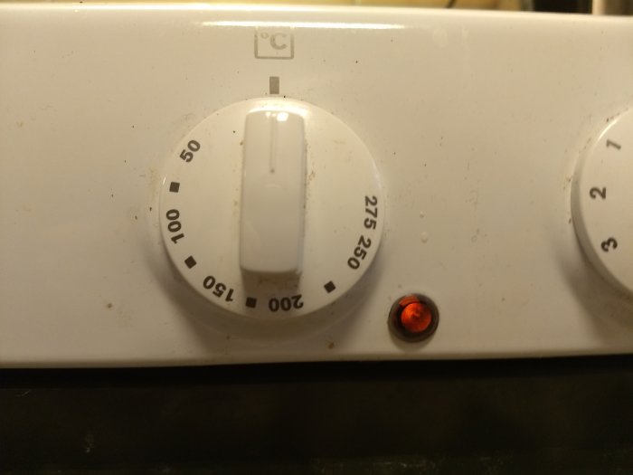 Närbild på gamla spisens vred och termostatindikator med en lysande röd lampa.
