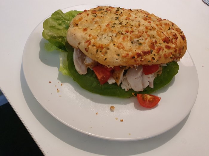 Tomatpanini med vitlök och örter, hjärtsallad, körsbärstomater, kryddig kyckling på en vit tallrik.