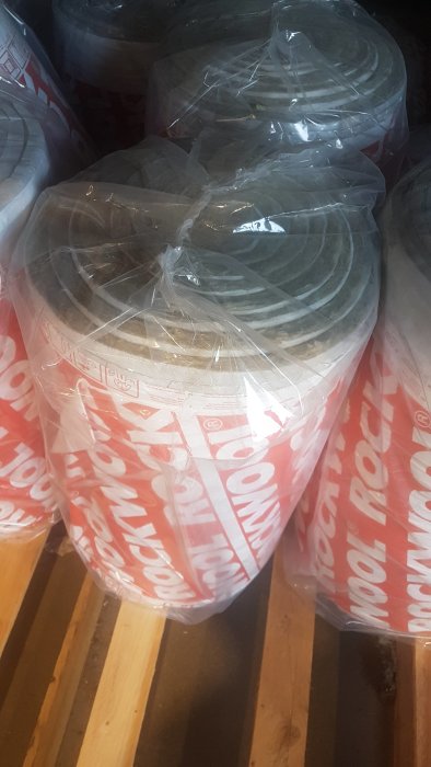 Flertalet förpackade Rockwool isoleringsrullar staplade på en träpall.