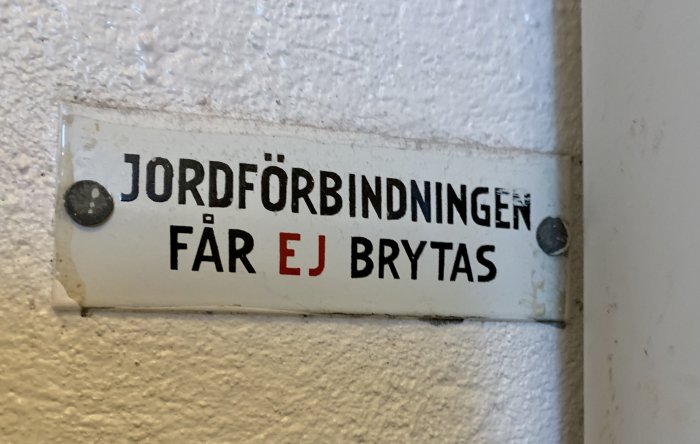 Skylt som säger "Jordförbindningen får ej brytas" fastsatt på en vägg.